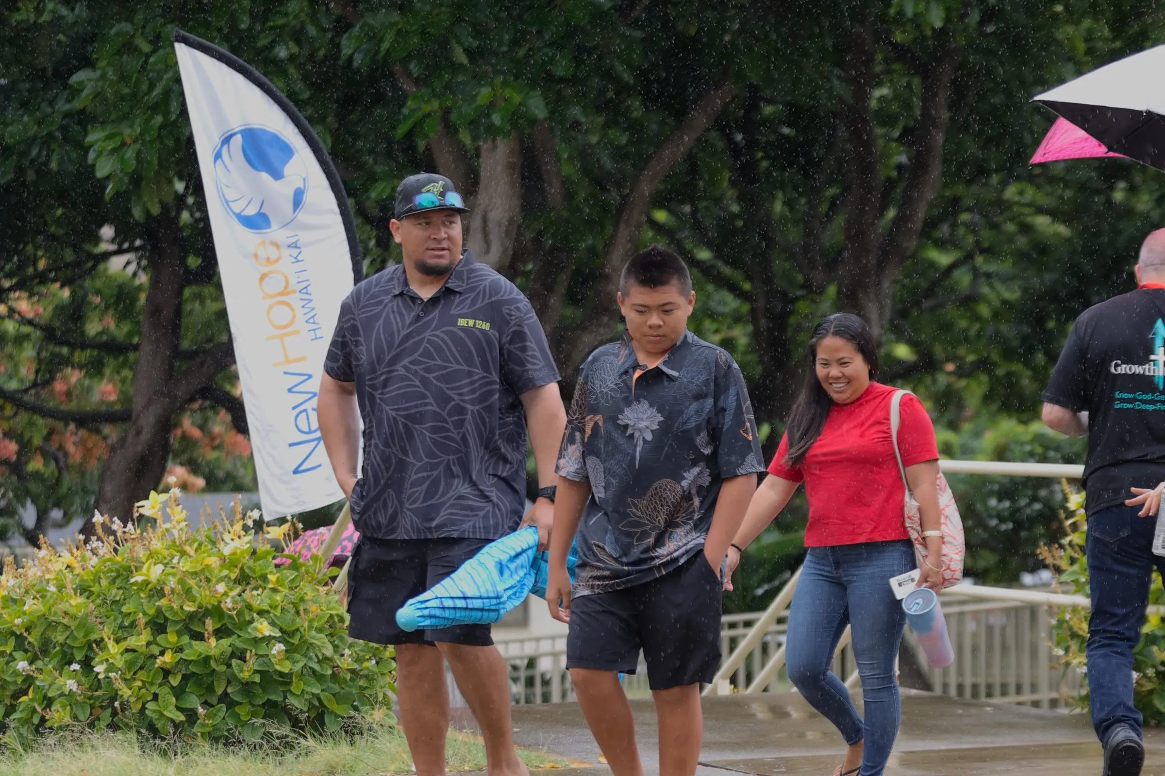 A family walking in past a New Hope Hawaii Kai banner at Kaiser High School on a rainy Sunday