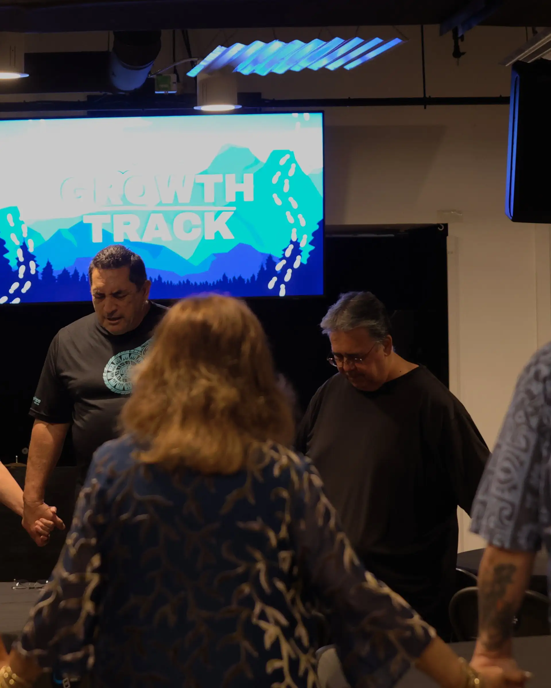 A small group at New Hope Hawaii Kai stands in a circle with heads bowed, praying together