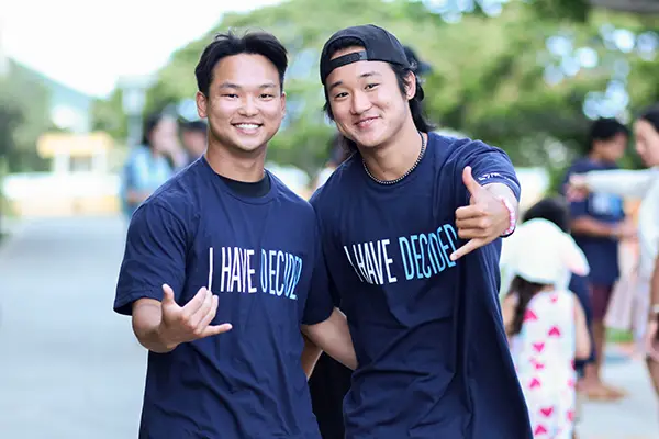 Two smiling young men in navy I Have Decided shirts giving shakas