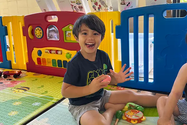 A toddler laughing with both hands up in the Children's Ark nursery