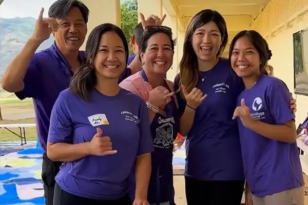 Five Children's Ark volunteers in purple shirts grinning and giving shakas