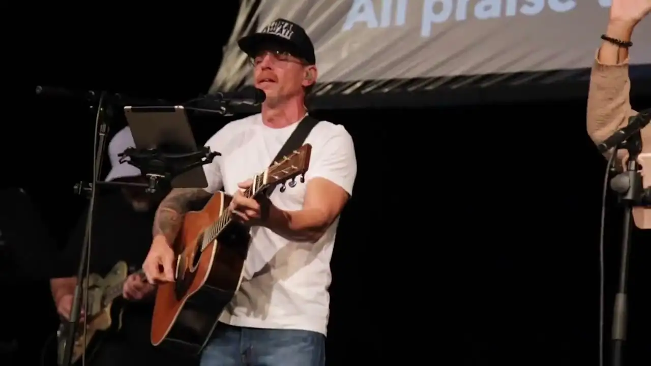 A worship leader with an acoustic guitar leading the room in song on a Sunday morning