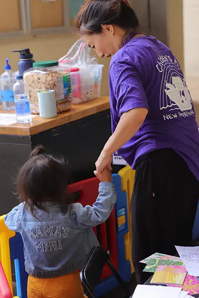 A Children's Ark volunteer holding a toddler's hand at the check-in table