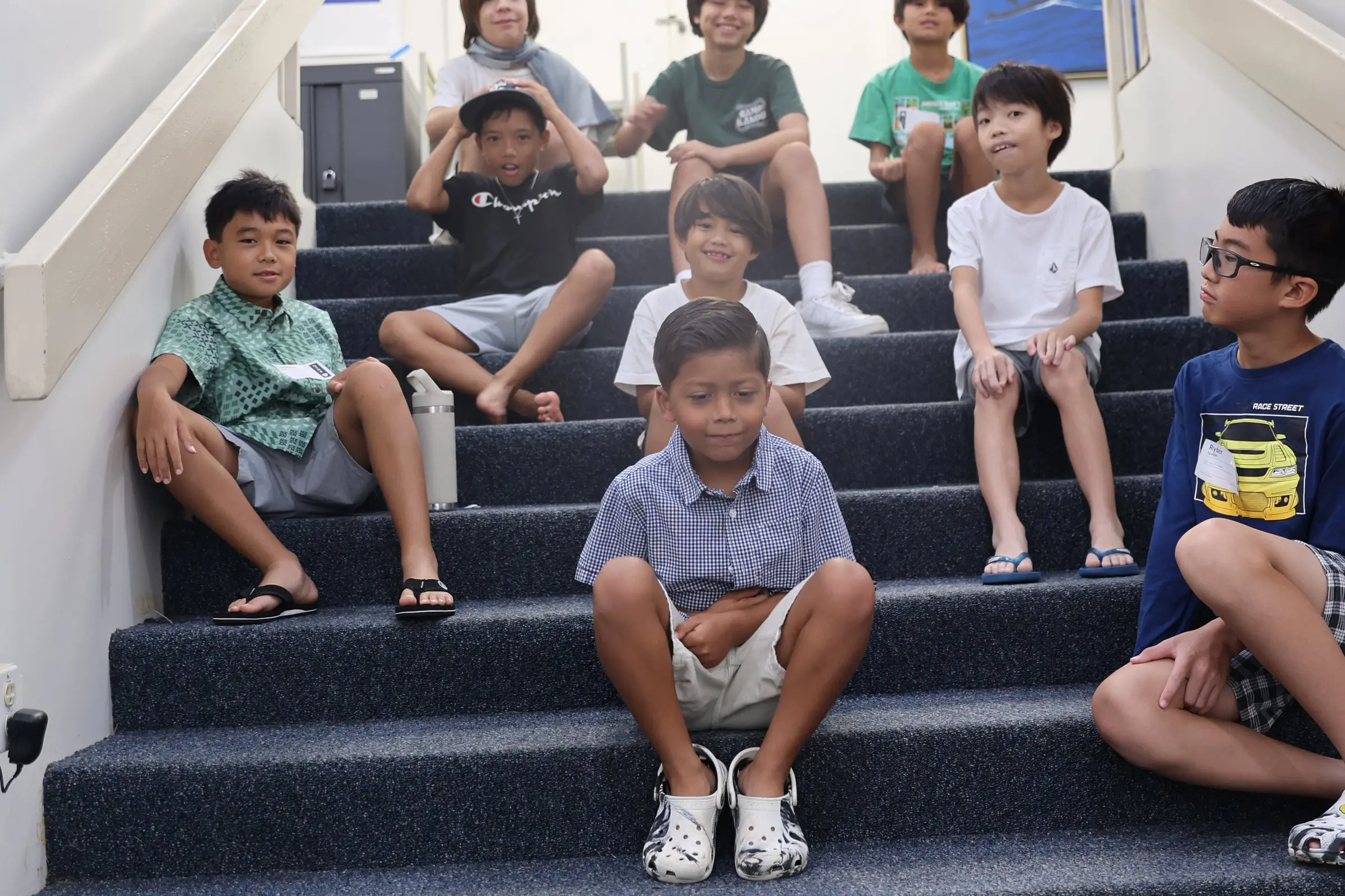 A group of grinning kids hanging out together on a carpeted staircase