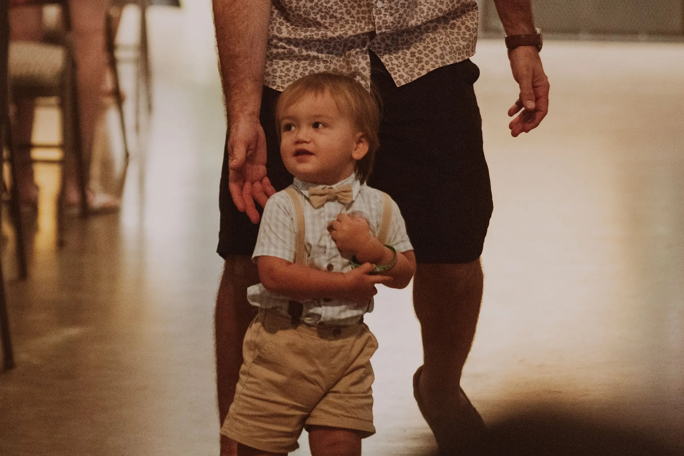 A toddler in a bow tie walking down the aisle holding his dad's hand