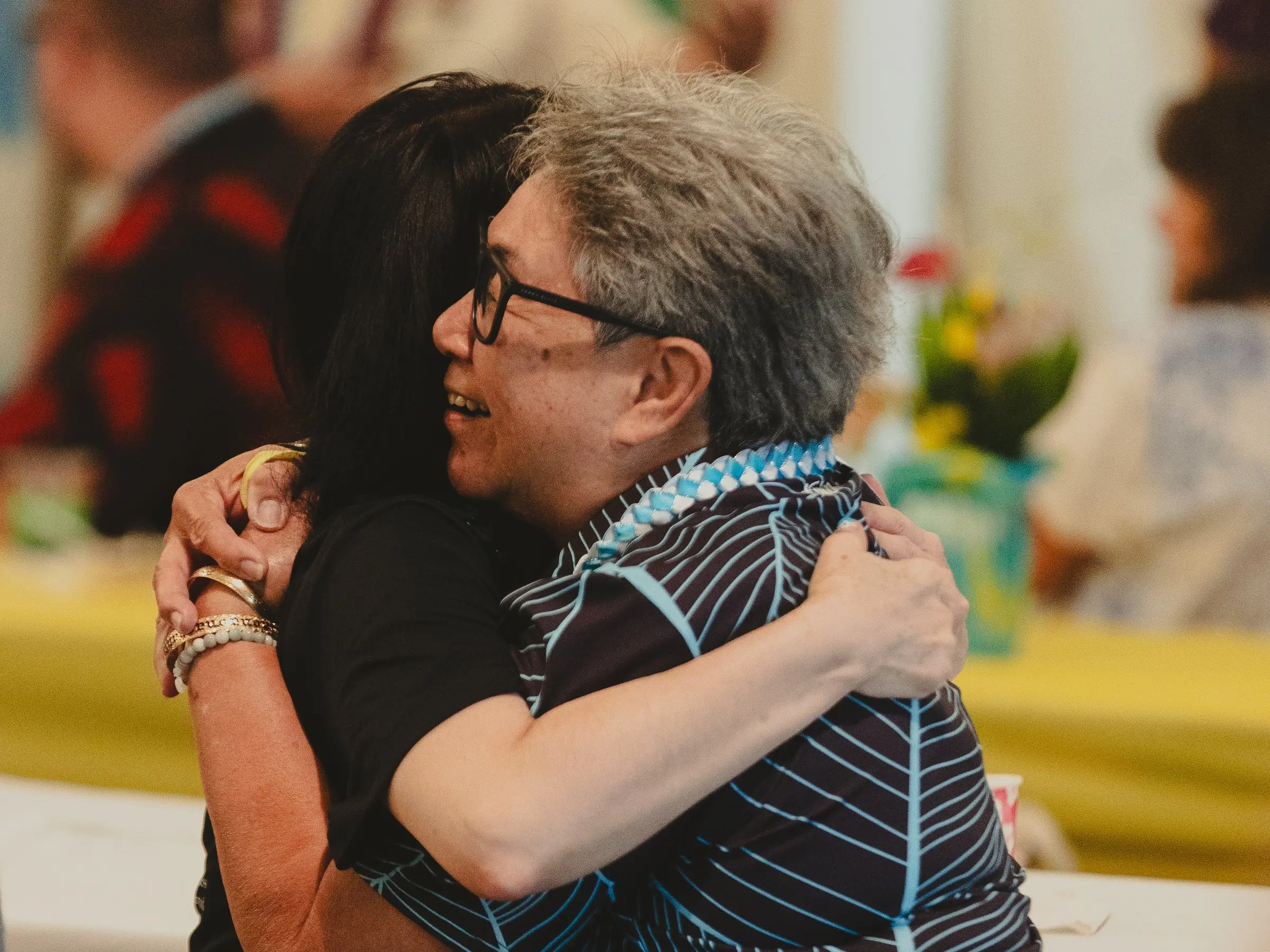 Two women in leis sharing a big hug at a church celebration