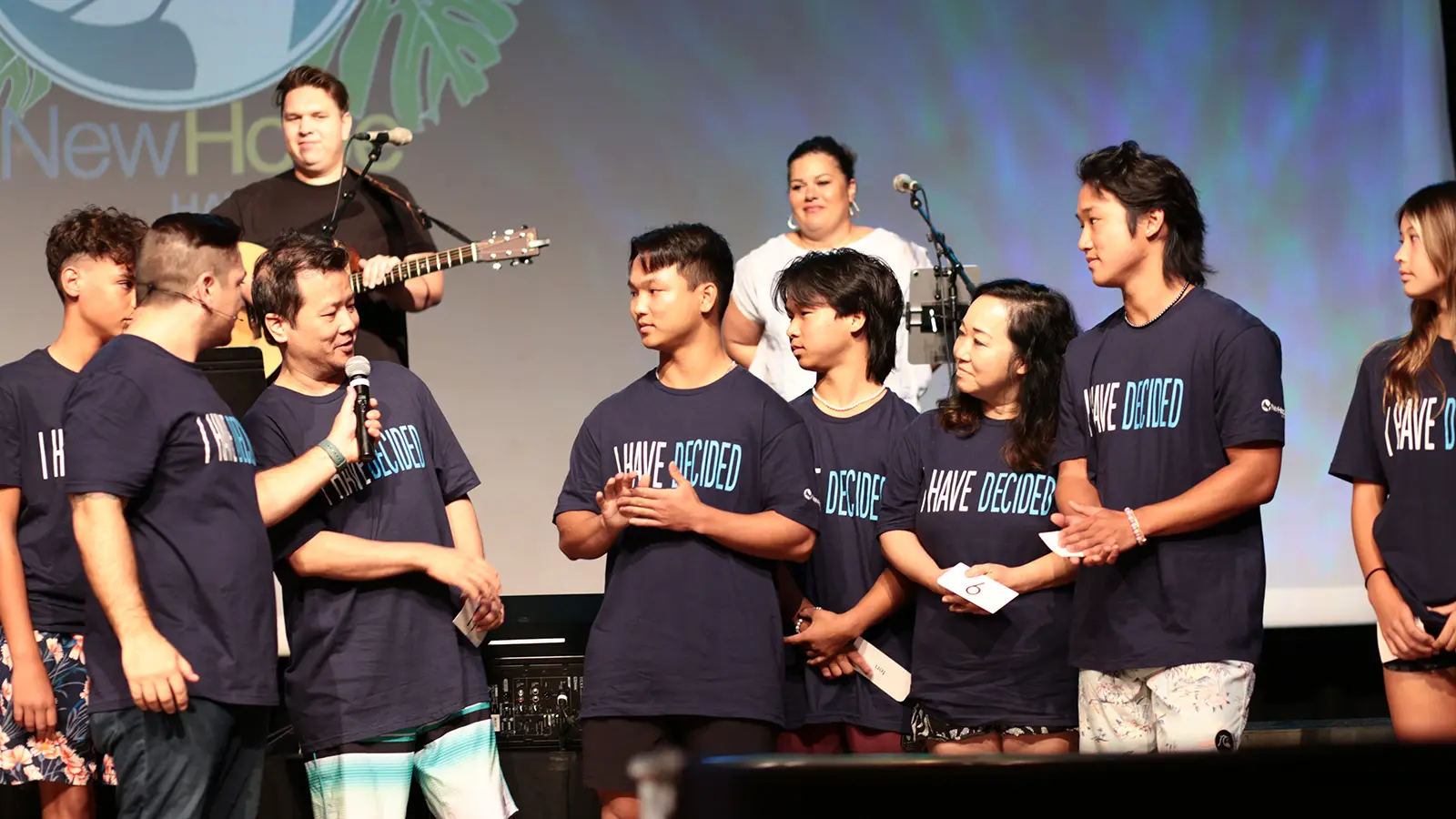 New Hope Youth students in matching I Have Decided shirts on stage with a leader holding a mic